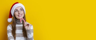 Sarı arka planda Noel Baba şapkalı gülümseyen genç kadın. Pankart.