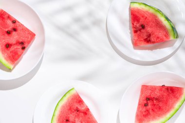 Beyaz bir masada beyaz tabaklar üzerinde olgun karpuz dilimleri. Üst manzara, düz uzanma.