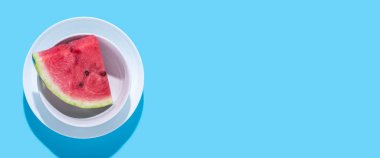 Mavi arka planda bir tabakta sulu kırmızı karpuz dilimi. Üst manzara, düz yatış. Pankart.