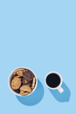Bir fincan kahve, mavi arka planda bir kasede kurabiyeler. Üst manzara, düz uzanma
