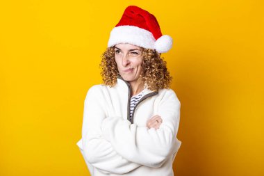 Sarı arka planda Noel Baba şapkalı sinirli kıvırcık kadın.