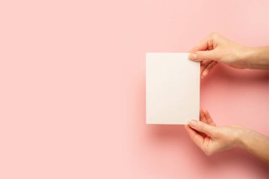 Pastel pembe arka planda bir kart tutan kadın eller. Pankart. Düz yatış, üst görünüm.