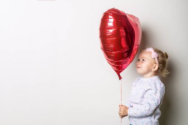 Arka planda kalp şeklinde bir balon tutan küçük bir kız. Sevgililer Günü konsepti, doğum günü. Pankart.