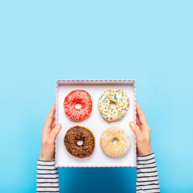 Kadın eli mavi arka planda donutlu bir kutu tutuyor. Şekerleme dükkanı, hamur işleri, kahve dükkanı. Pankart. Düz yatış, üst görünüm.