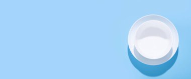 Temiz beyaz tabaklar, mavi arka planda tabaklar. Üst manzara, düz yatış. Pankart.