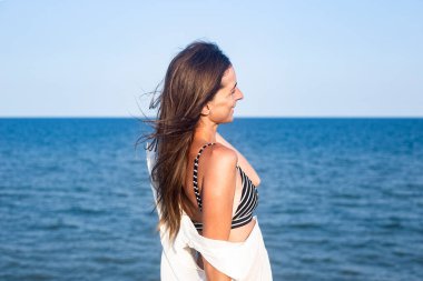 Güzel, seksi bir kadın, hafif bir pareo ile kayalıklarda denize bakıyor. 