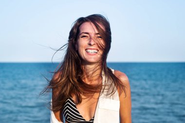 Denizin arka planında mayo giymiş neşeli, genç bir kadın. 