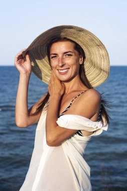 Bir yaz günü denizin arka planında şapkalı güzel bir kadın gülümsüyor. 