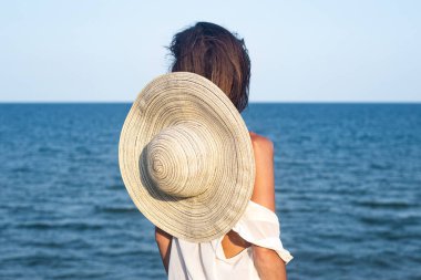 Sırtında şapkasıyla denizde oturan genç bir kadın.