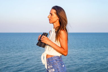 Uçurumun kenarında dürbünlü bir kız okyanusun arka planında 