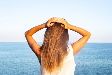 Genç bir kadın avuçlarını denizin arka planına dayayarak yüzünü güneşten korur. 