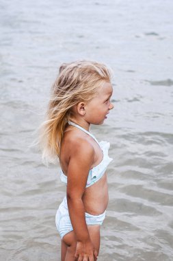 Bronzlaşmış mayo giymiş çocuk denizde mayo giyiyor.
