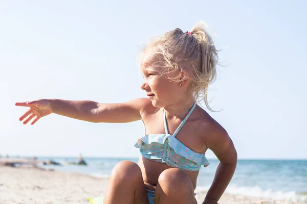 Niña Traje Baño Muestra Mano Lado Mientras Está Sentada Playa — Foto de Stock