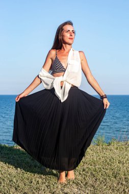 Uzun siyah etekli güzel bir kadın uçurumun kenarında dikilirken poz veriyor. 