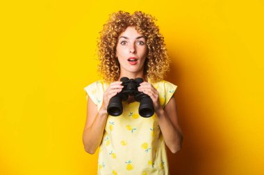 Sarı arka planda, önünde dürbün tutan genç bir kadın.