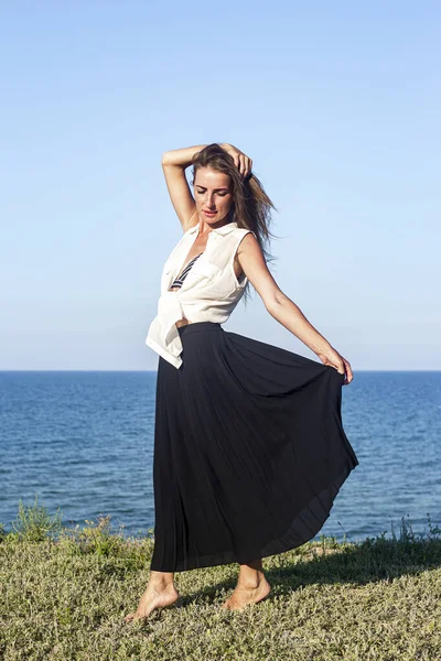 Uzun siyah etekli güzel bir kadın uçurumun kenarında dikilirken poz veriyor. 