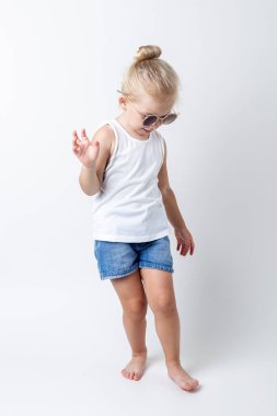 Güneş gözlüklü sarışın çocuk stüdyoda arka planda poz veriyor..