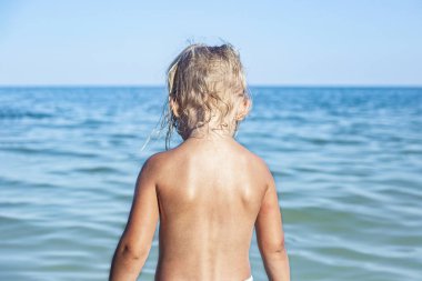 Çocuk kız sırtı dönük sahilde denize bakıyor. 