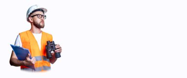 Dürbünlü, ışıklı arka planda bir panosu olan, inşaat kıyafetleri giyen genç bir adam. Pankart