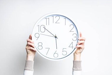 Kadın eller arka planda büyük beyaz bir saat tutuyor. 