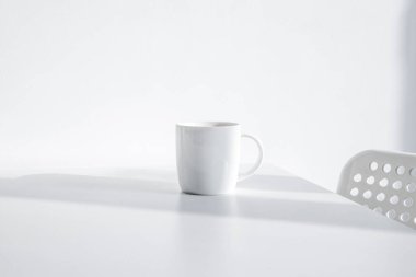 Beyaz bir masada, doğal ışık altında beyaz bir fincan.