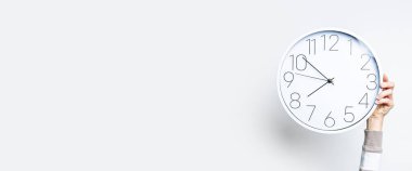 Kadının eli, ışık duvarına karşı büyük beyaz bir saat tutuyor. Pankart