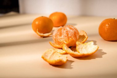 Bej bir arka planda güneş ışığı altında taze mandalinalar.