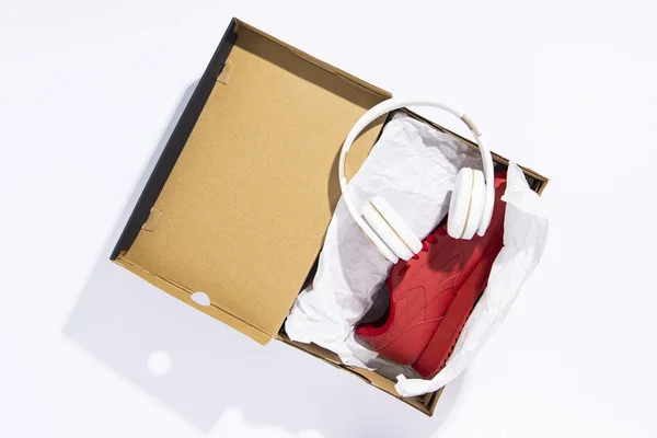 Koptelefoons Liggen Een Doos Met Nieuwe Sneakers Een Rode Achtergrond — Stockfoto