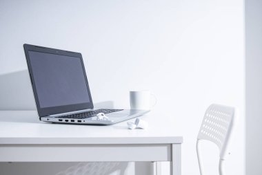 Laptop, fincan, beyaz bir masada kablosuz kulaklık. Serbest İşyeri 