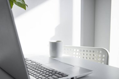 Laptop, beyaz masadaki beyaz kahve bardağı. Serbest İşyeri 