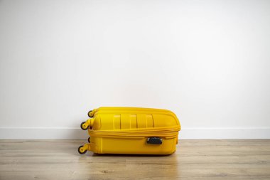 Sarı bavul ahşap bir zeminde beyaz bir duvara karşı. 