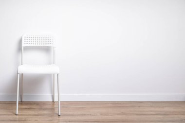 Beyaz plastik sandalye tahta bir zeminde beyaz bir duvara karşı duruyor. 