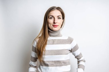 Hafif arka planda çizgili süveter giyen doğal makyajlı genç bir kadın.