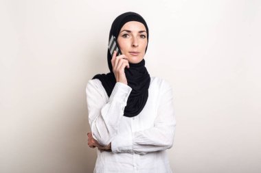 Tesettürlü genç Müslüman bir kadın telefonda konuşuyor ve arka planda kameraya bakıyor. Pankart.