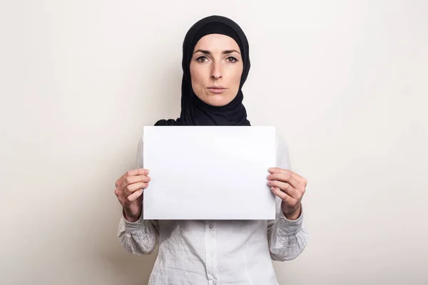 白いシャツを着た若いイスラム教徒の女性と悲しい顔をしたヒジャーブは 空白の紙を持っています テキストの場所 バナー — ストック写真
