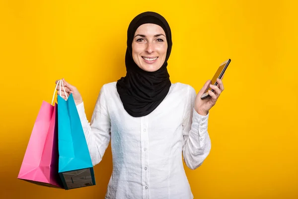 Surpreendido Jovem Muçulmana Hijab Detém Sacos Compras Telefone Fundo Amarelo — Fotografia de Stock