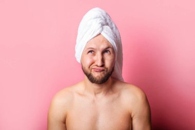 Pembe arka planda kafasında havluyla düşünceli genç bir adam..