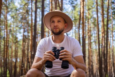 Kamp gezisi sırasında şapkalı bir adam dürbün tutuyordu. Dağlarda yürüyüş, orman....