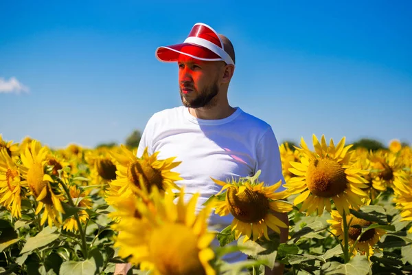 Young man in a red sun shade on his head on a sunflower field on a clear day.