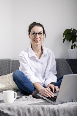 Kanepede otururken dizüstü bilgisayarlı, gülümseyen genç kadın.