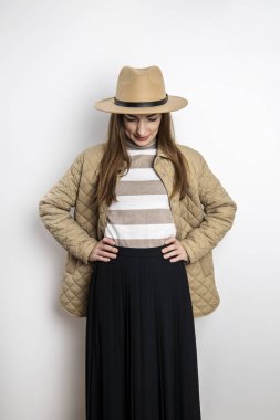 Beyaz bir duvarın arkasına yaslanmış, şapkalı genç bir kadın.