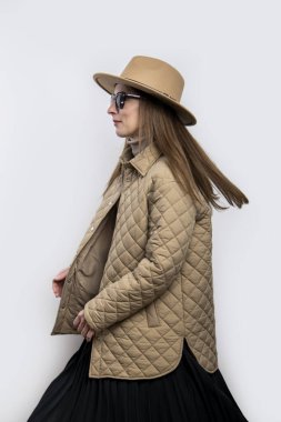 Beyaz bir duvarın arkasında şapkası olan ceketli genç bir kadın. 