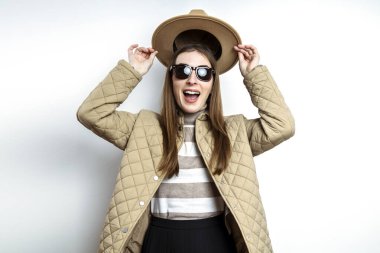 Ceketli gülümseyen genç kadın beyaz bir duvarın arkasında şapkasını çıkardı. 