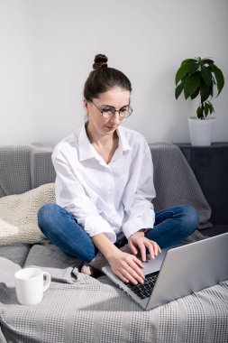 Dizüstü bilgisayarlı, kanepede kahve içen genç bir kadın.