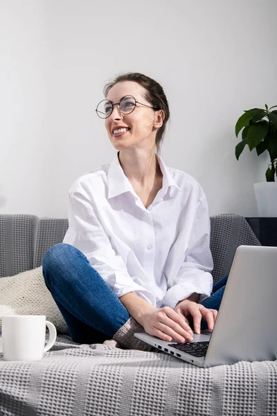 Kanepede oturan dizüstü bilgisayarlı gülümseyen genç kadın.