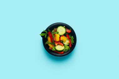 Plastik bir tek kullanımlık kasede açık mavi arka planda sebze salatası. Üst manzara, düz uzanma.