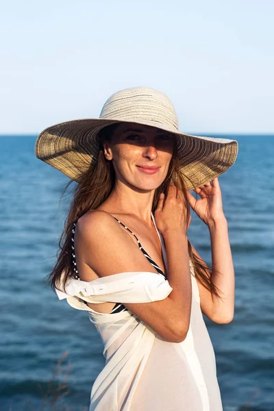 Gülümseyen, güzel, seksi, şapkalı bir kadın denizin arka planında.