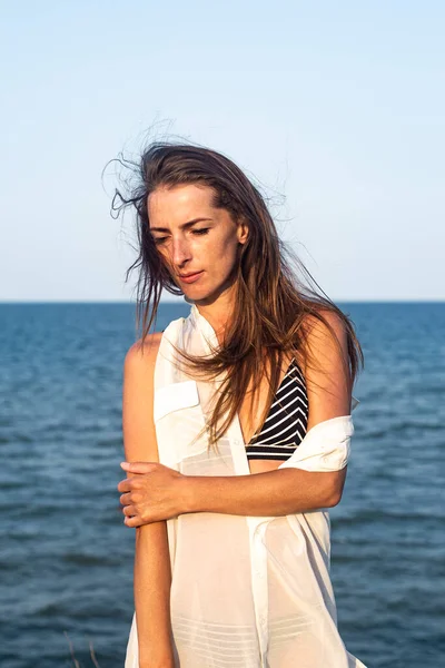 Denizin arka planında hafif bir pareo giymiş güzel genç bir kadın.