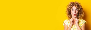 frightened surprised curly young woman holding clenched fists on yellow background. Banner