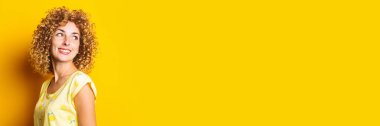 smiling cute curly girl looks back on a yellow background. Banner